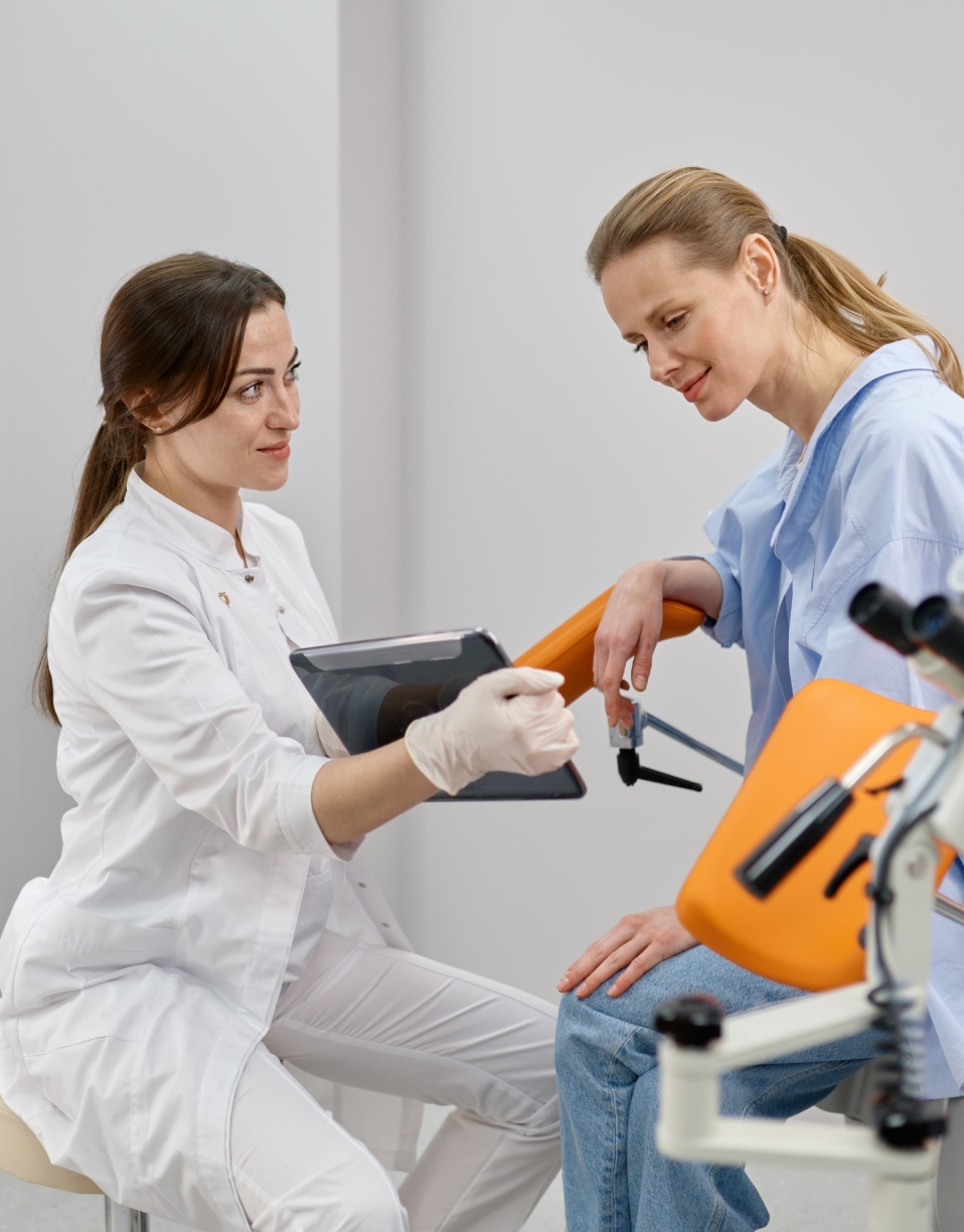 Médecin consultant une tablette avec une patiente assise sur un appareil médical | hystero sono salpingosongraphie | Notre vision | Imagerie Cardinet | Région Parisienne